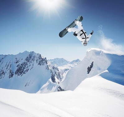 snowboarder backflipping off a backcountry jump in the sun